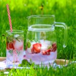 glass and pitcher of infused water with strawberries and mint on grass