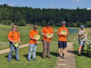 Four youths stand on a gun range holding certificates.