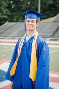 A young man standing on a football field in a graduation cap and gown.