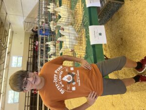 A boy stands beside chickens displayed in a cage.