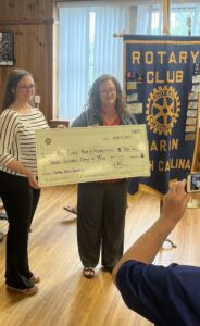Two women hold a large check beside a banner that reads Rotary Club.